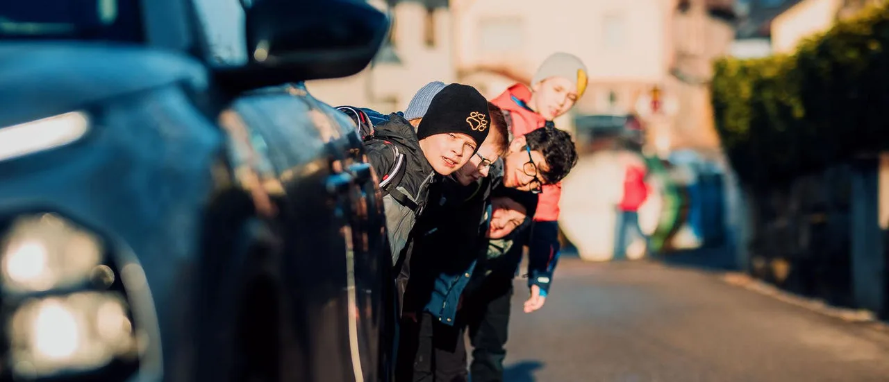 Kinder auf dem Schulweg hinter einem Auto